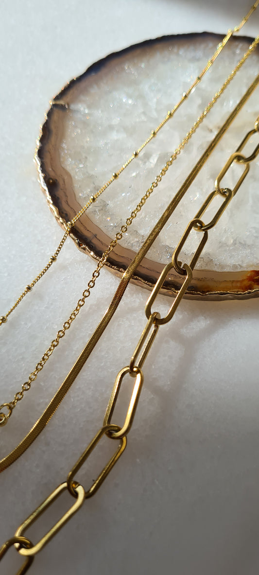 3 gold necklaces of different styles laid in a line across a quartz stone